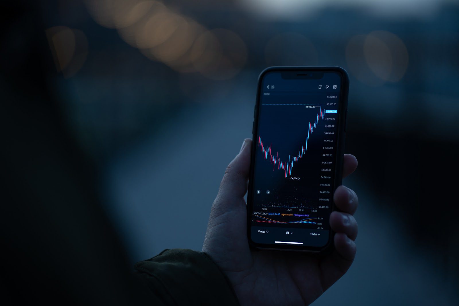 Businessman or trader using mobile phone to check real time stock market data while standing outdoors, selective focus on male hand holding smartphone with forex graph chart